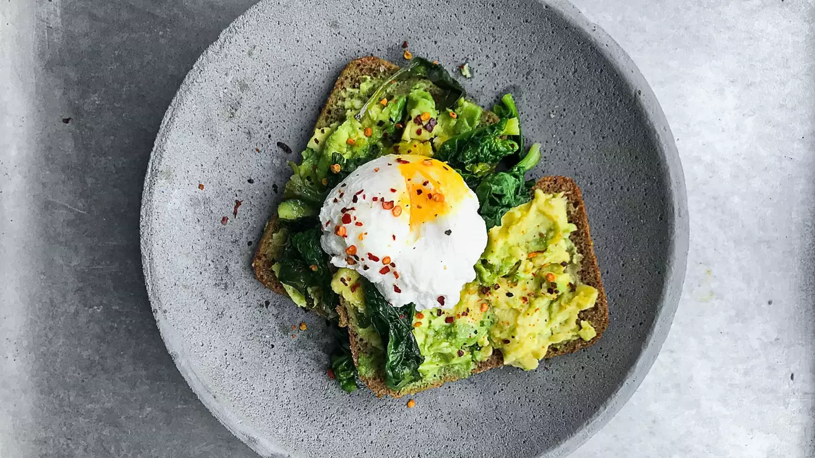 stone bowl containing avocado toast and a poached egg on top